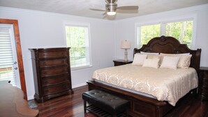 Un dormitorio con cama de madera, una banca, cómoda y ventilador de techo.