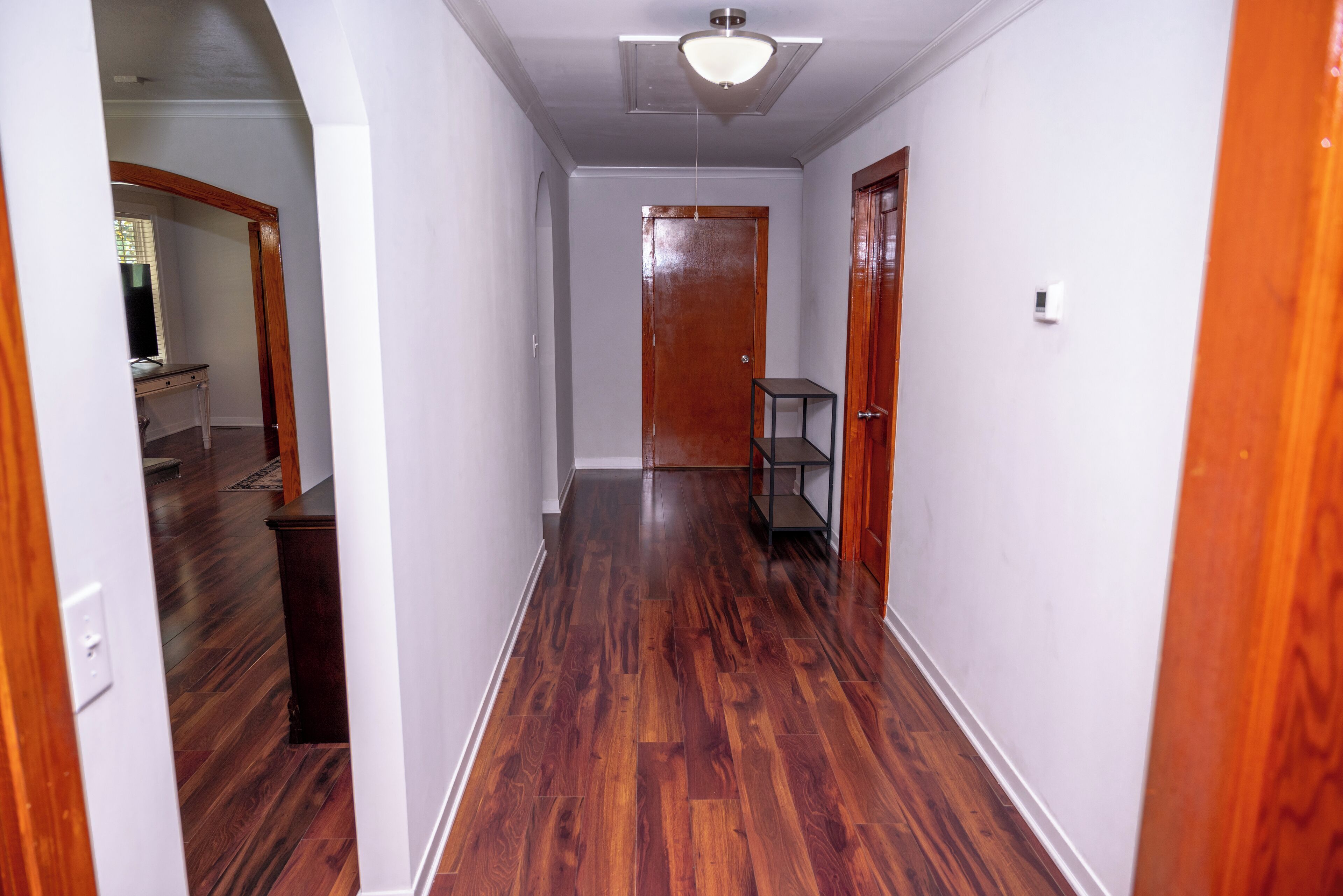 A hallway with wooden flooring, white walls, and a ceiling light fixture.