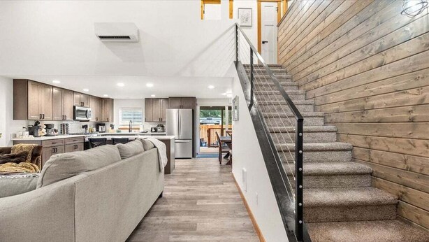 A modern kitchen with wooden cabinets, a grey sofa, and a staircase with a metal railing. - Perch - Spacious Modern Cabin w/ Hot Tub, BBQ & Cali- King-Sized Bed | Pet-Friendly (Ashford)