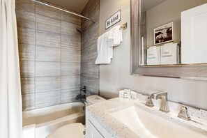 A modern bathroom with a shower, a bathtub, and a sink with a mirror. There are towels hanging on the wall and a sign that says "Be kind". - Family-friendly, soundfront getaway with deck, Wifi, W/D and mountain views (Fox Island)
