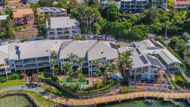 An aerial view of a coastal hotel with multiple buildings, a clear waterfront, and a pedestrian bridge. - Waterfront at Sunrise Cove (Kingscliff)
