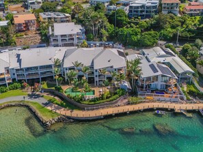 An aerial view of a coastal hotel with multiple buildings, a clear waterfront, and a pedestrian bridge. - Waterfront at Sunrise Cove (Kingscliff)