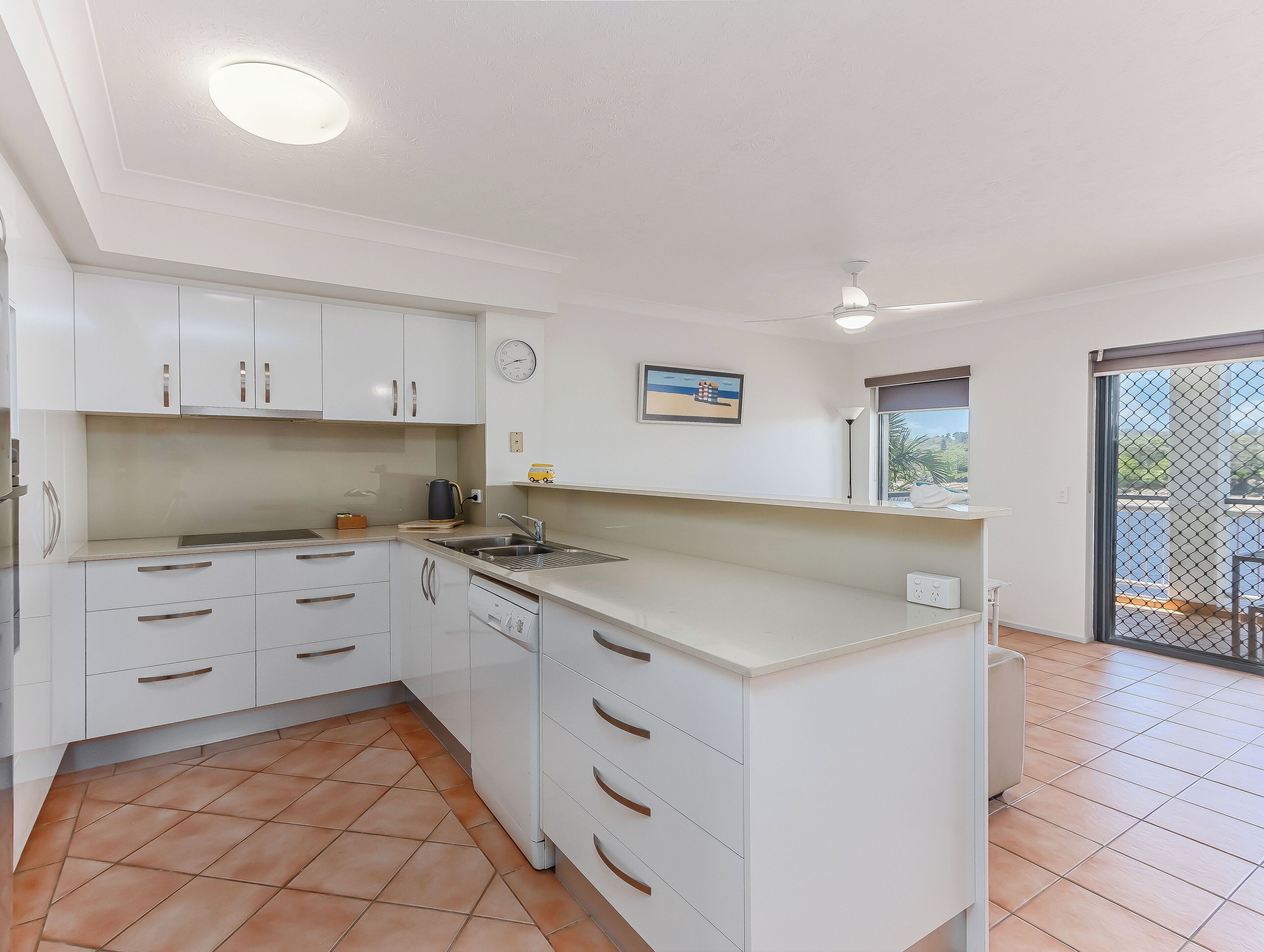A modern kitchen with white cabinets, a sink, and a clock on the wall.