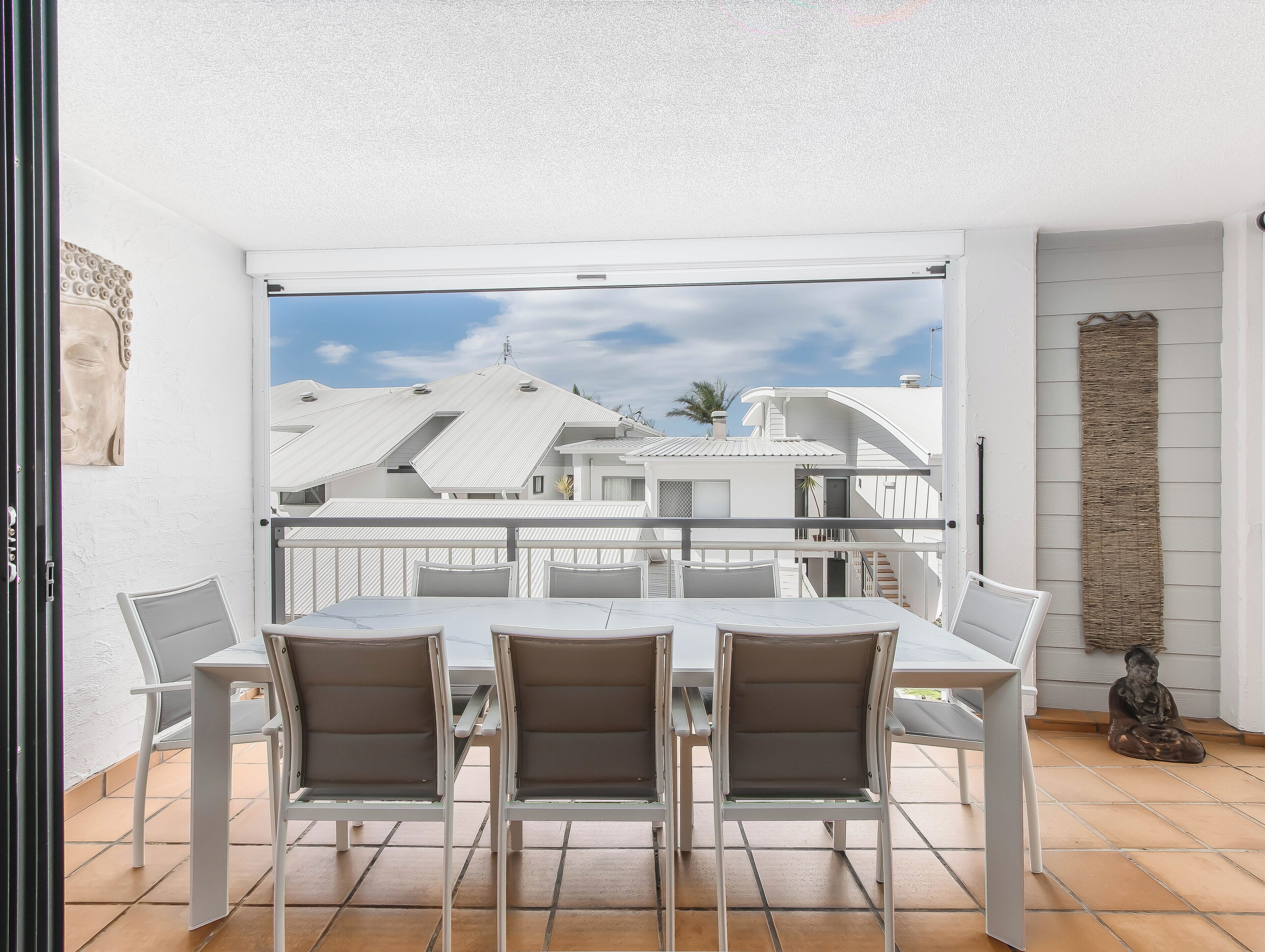 A balcony with a white table and chairs, a view of white buildings, and a stone wall.