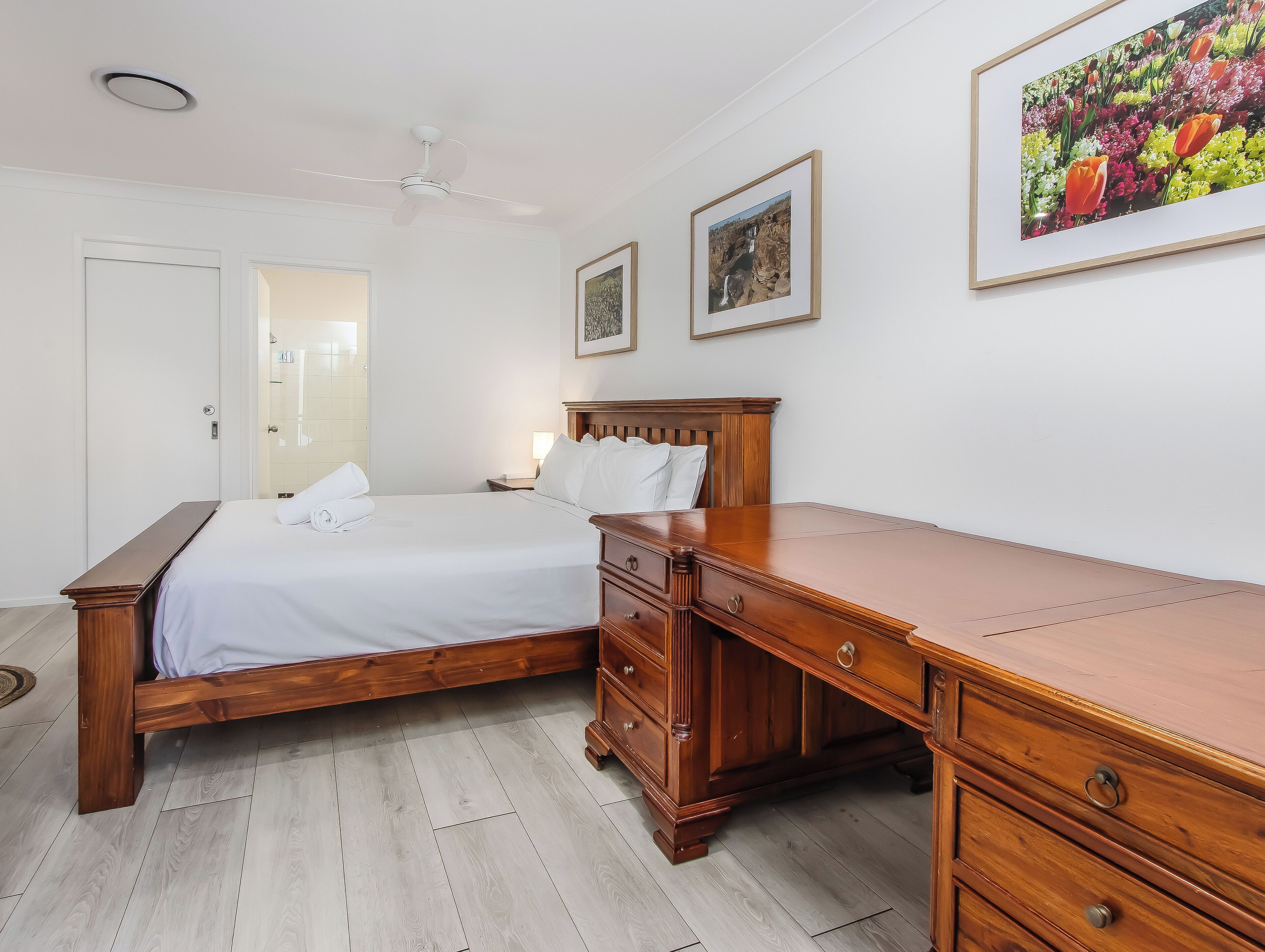 Una camera da letto con un letto di legno, un comodino, una scrivania e una ventola a soffitto.
