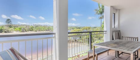 A balcony with a table and chairs, overlooking a body of water and greenery.