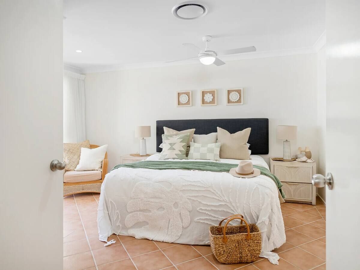 A bedroom with a bed, a nightstand, a chair, a ceiling fan, and a wall-mounted light fixture.