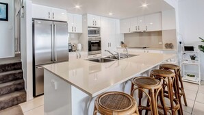 A modern kitchen with white cabinetry, stainless steel appliances, and a central island with bar stools. - Waterfront at Sunrise Cove (Kingscliff)