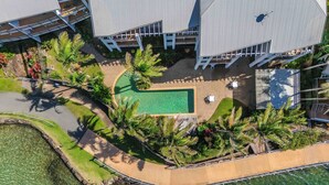 An aerial view of a resort with a swimming pool, palm trees, and a curved walkway. - Waterfront at Sunrise Cove (Kingscliff)