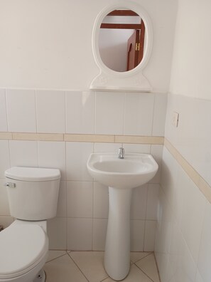 A compact bathroom with a toilet, pedestal sink, and mirror.