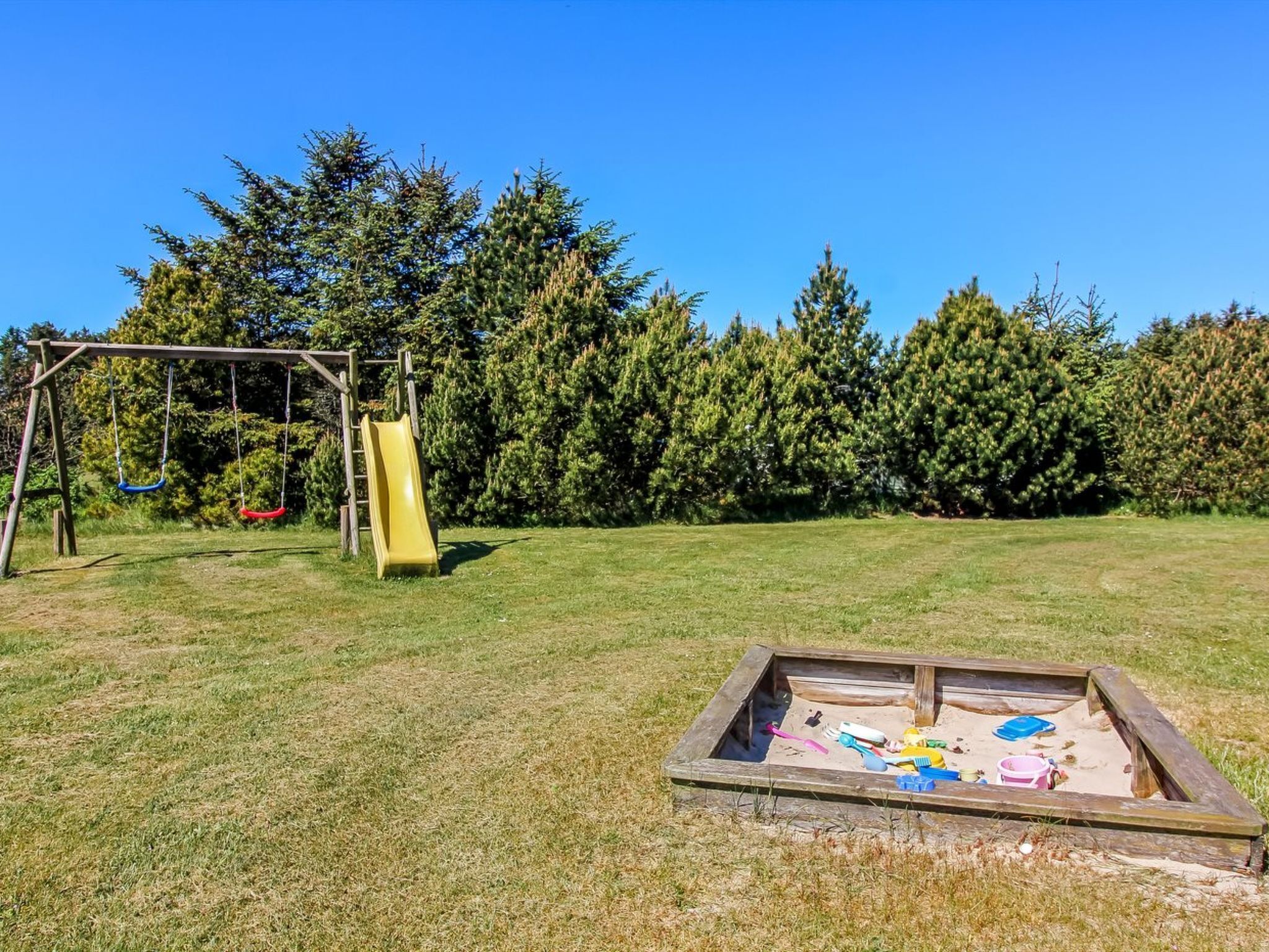Un'area giochi con scivolo e altalene, immersa nel verde tra prati e alberi fitti.