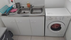 Un espace buanderie compact comprenant un lave-linge, deux éviers, un étendoir et une petite poubelle.