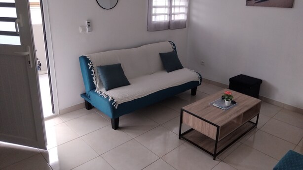 A living room with a blue sofa, a coffee table, a hanging plant, and a beach scene painting.