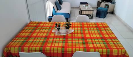 A dining area with a table covered by a plaid tablecloth, two white chairs, and a small table with a vase of flowers.