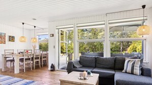 A modern living room with a wooden floor, a grey sofa, a wooden coffee table, and large windows offering a view of greenery. - "Aldina" - 400m to the fjord by Interhome (Havndal)