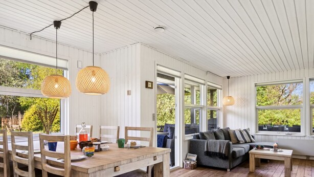 A spacious living area with a wooden dining table, two hanging wicker lamps, a grey sofa, and a view of the outdoors through large windows. - "Aldina" - 400m to the fjord by Interhome (Havndal)