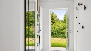 Un pasillo moderno con un amplio ventanal que da a un jardín, lavadora integrada y un perchero de pared.