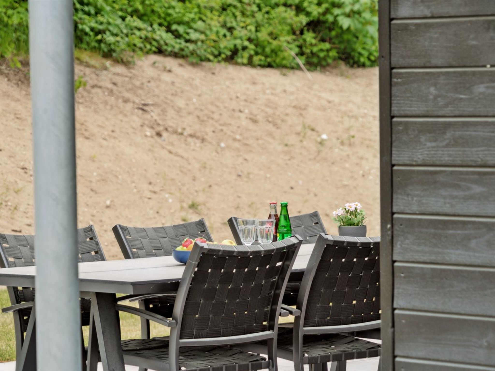 An outdoor dining area with a table and chairs, a bowl of fruit, and bottles of beverages.