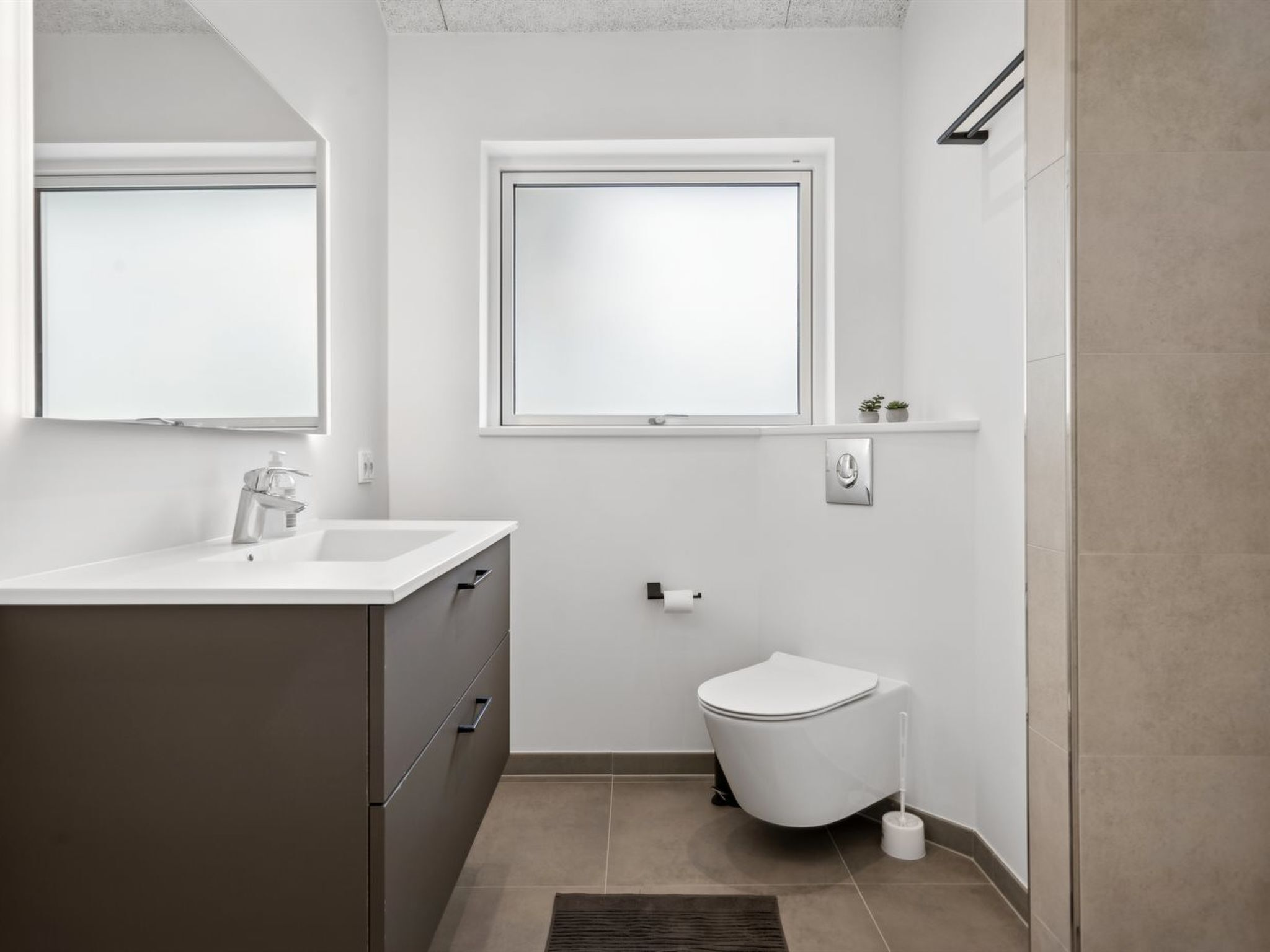 Un bagno moderno con un mobile lavabo bianco, un water e una finestra.