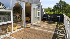 A modern house with a wooden deck, large sliding glass doors, and outdoor furniture.