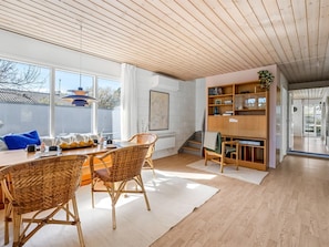 Un interior moderno con zona de comedor, techo de madera y una estantería.