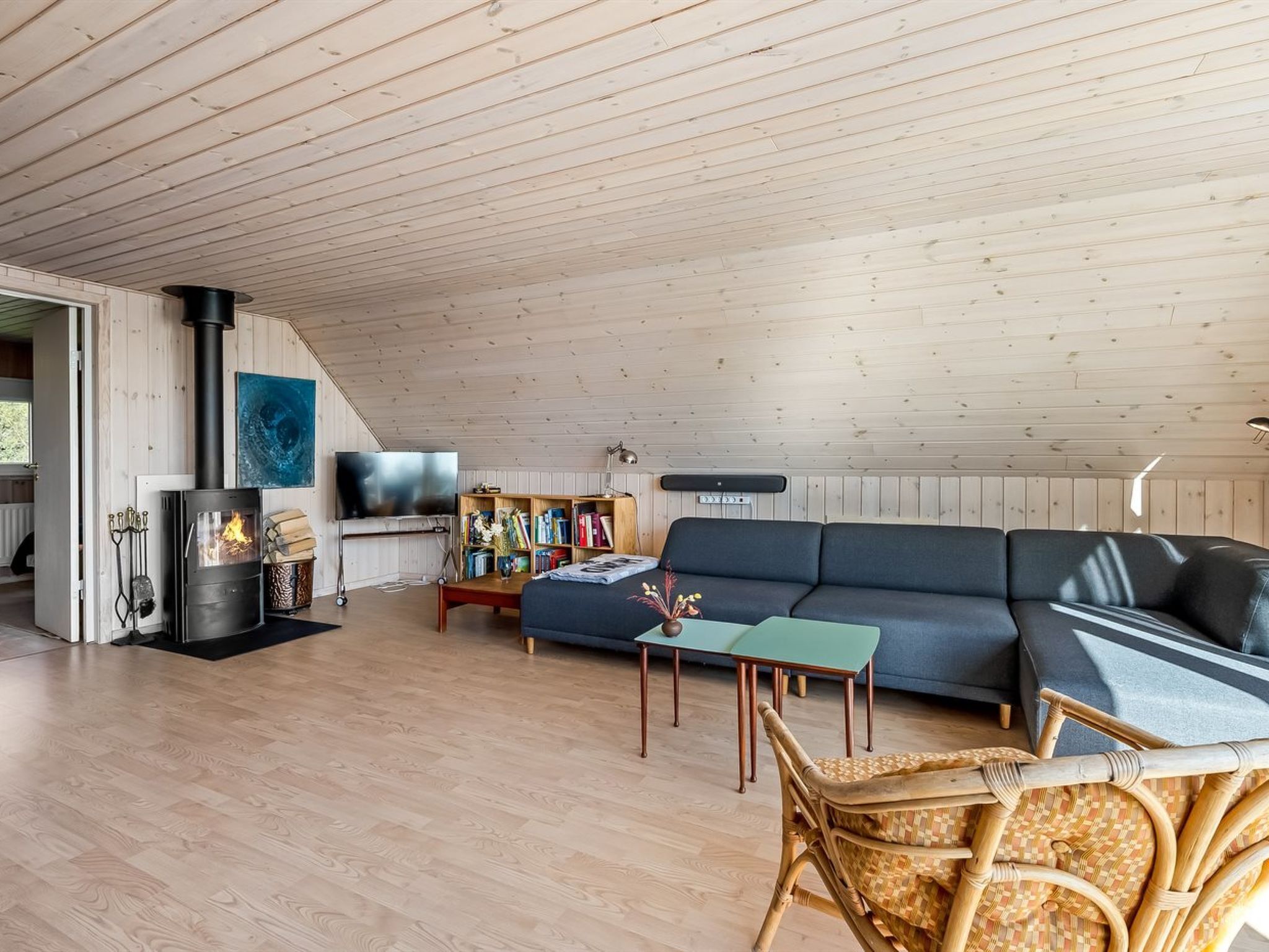 A cozy loft-style living room with a wooden ceiling, a black sofa, a television, a bookshelf, and a fireplace.