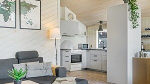 A modern living room with a grey sofa, a small table with a plant, and a kitchen area with white cabinets and a microwave.