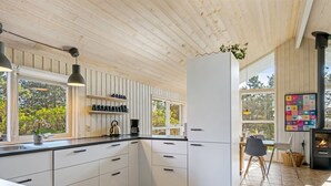 A modern kitchen with white cabinets, a stone tile floor, and a wood-paneled ceiling.