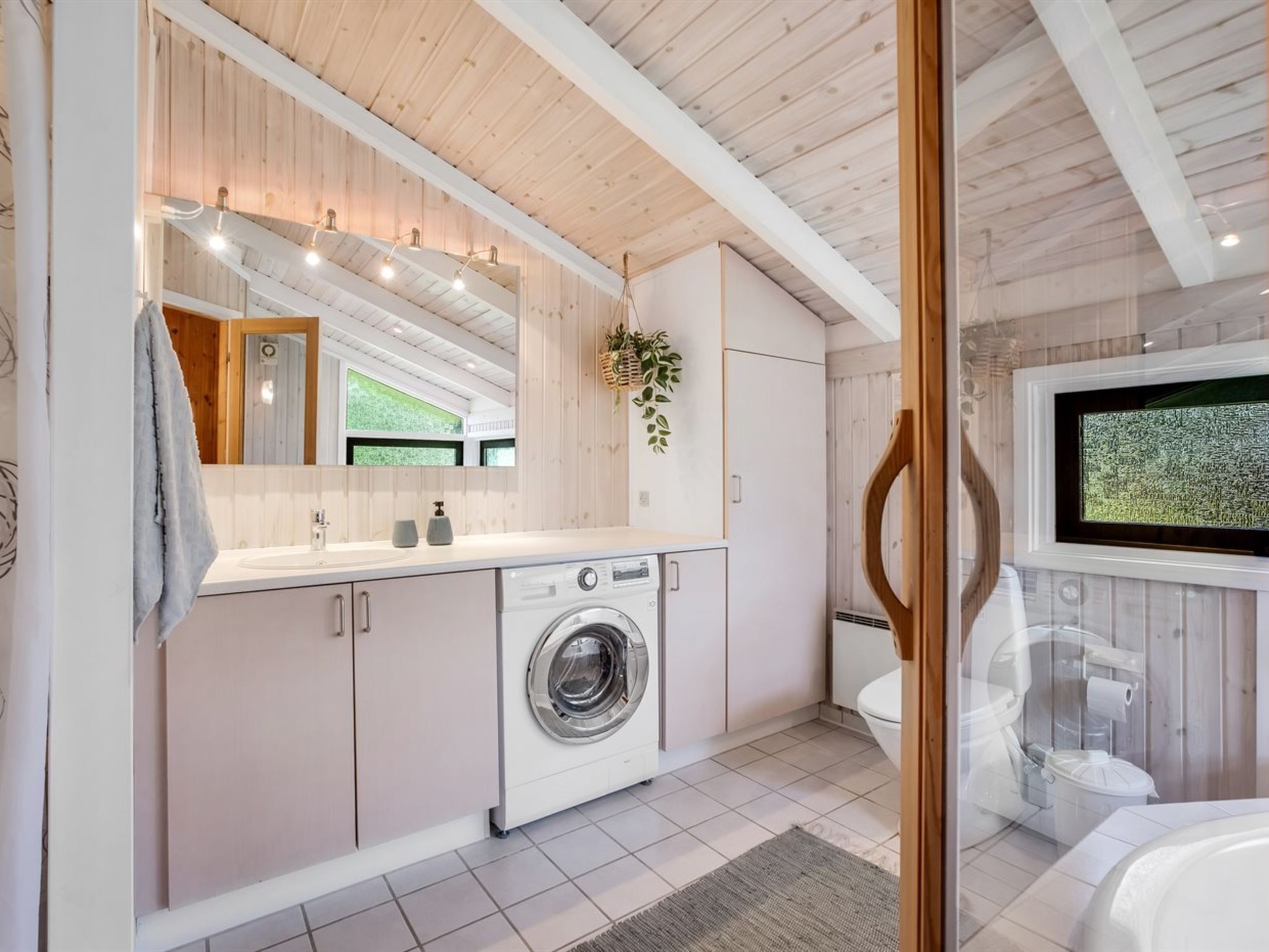 Ein modernes Badezimmer mit integrierter Waschmaschine, einem großen Spiegel und einem an der Wand befestigten Fernseher.