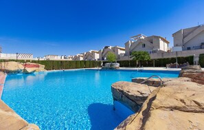 Une piscine d’un bleu éclatant, entourée de formations rocheuses et de bâtiments modernes.