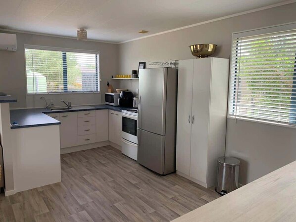 A modern kitchen with a built-in oven, a stainless steel refrigerator, and a sink. - Hosts on the Coast Charming on Charles (Cooks Beach)