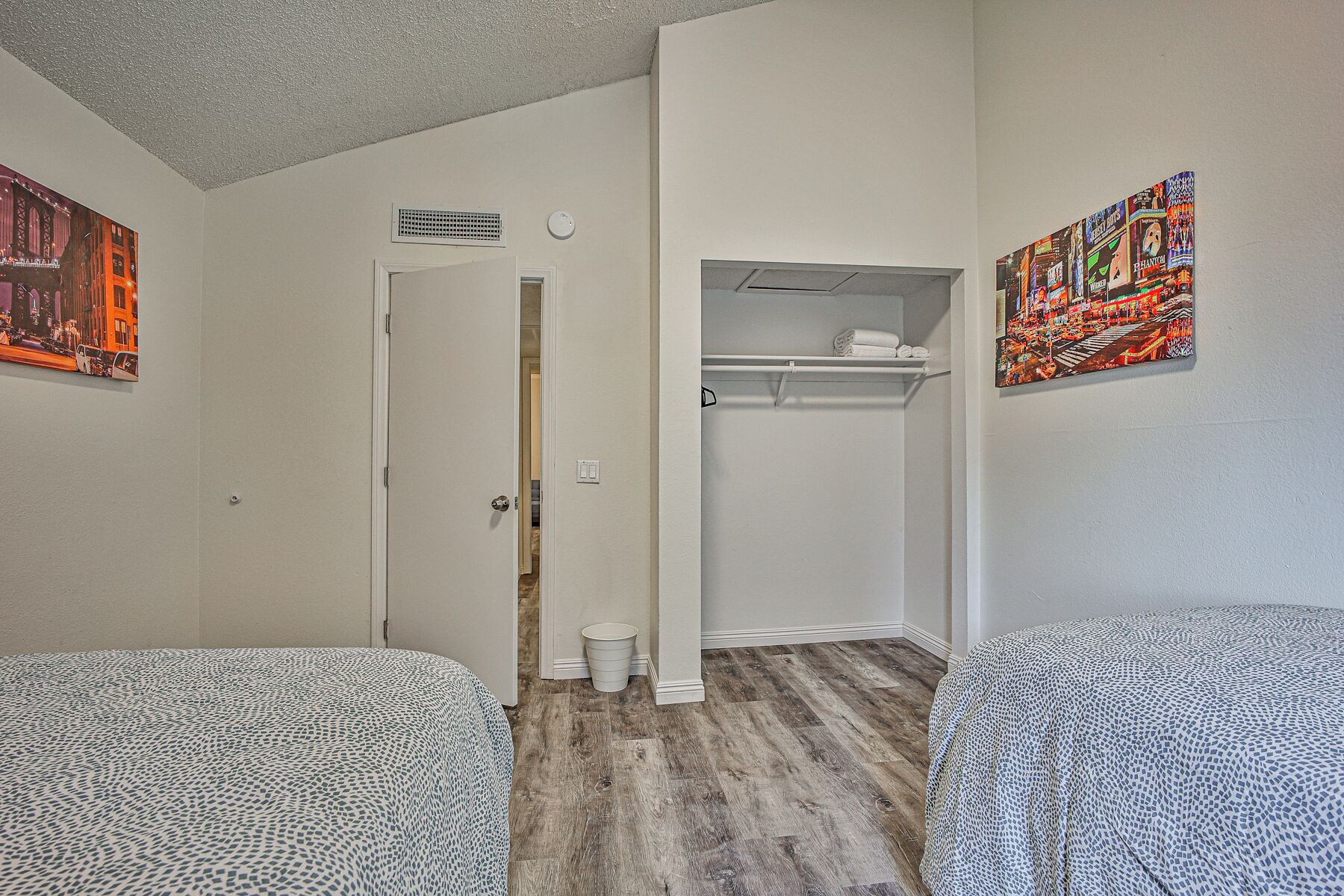 A hotel room with two beds, a closet with hanging clothes, a door leading to another room, and a wall with a colorful poster.