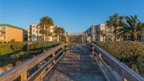A wooden boardwalk leading to a gated entrance with a view of modern buildings and palm trees. - Fully renovated in 2025!! (Saint Simons Island)