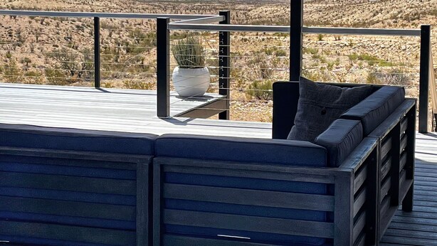 Un balcon donnant sur un paysage désertique, un coin salon avec des coussins et une plante en pot.