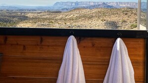 Un banc en bois, agrémenté de deux serviettes blanches, offre une vue sur un paysage rocheux avec des montagnes lointaines.