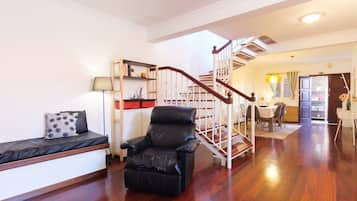 A spacious living room with a black leather sofa, a wooden staircase, and a dining area with a table and chairs.