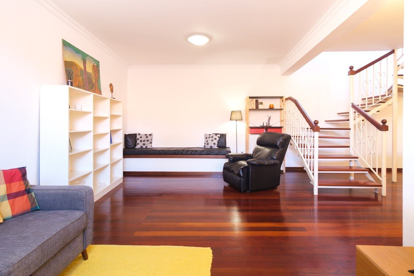 Un salon avec un canapé, un fauteuil en cuir noir, une bibliothèque et un escalier.