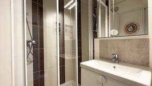 Un baño moderno con ducha de vidrio, un lavamanos blanco y un espejo con un diseño decorativo de sol.