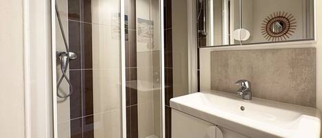 A modern bathroom with a glass-enclosed shower, a white sink, and a mirror with a decorative sunburst design.