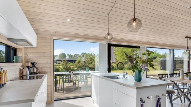 Eine moderne Küche mit einer großen Kochinsel, einem Essbereich mit Outdoor-Möbeln und großen Fenstern mit Blick ins Freie.