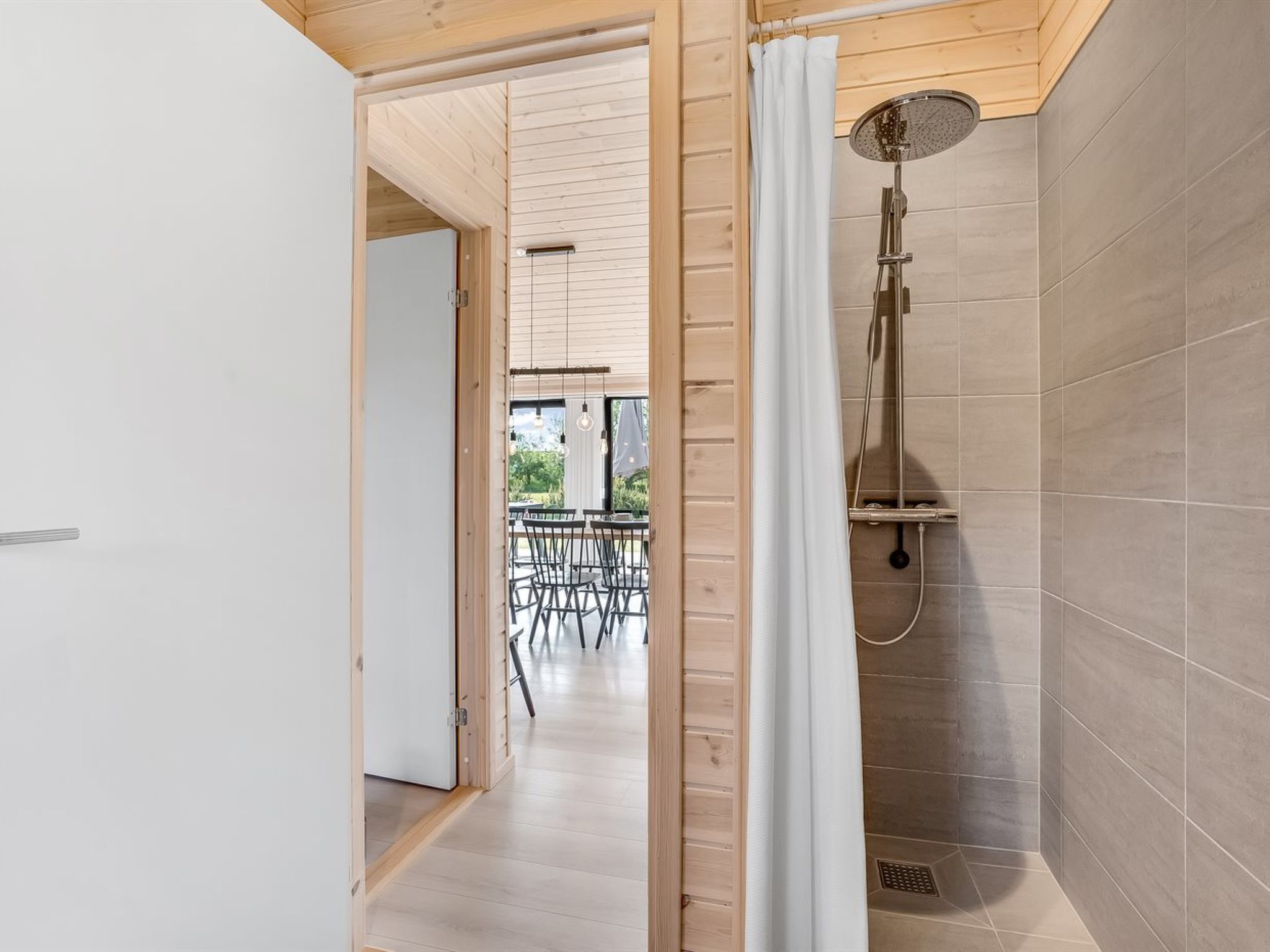 A modern bathroom with a shower, wooden flooring, and a view of an outdoor dining area.