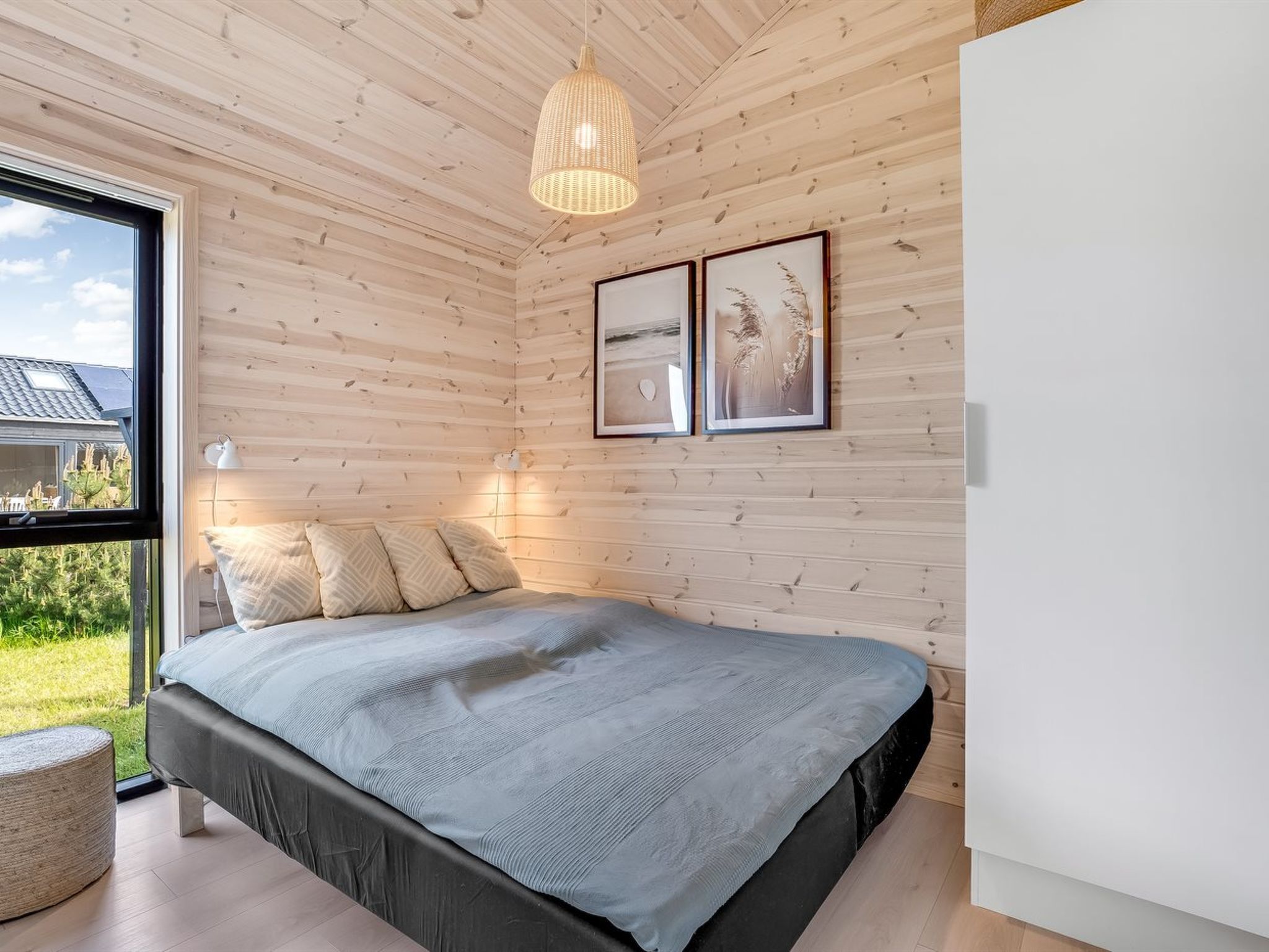 A bedroom with a bed, wooden walls, a hanging light fixture, and framed pictures on the wall.