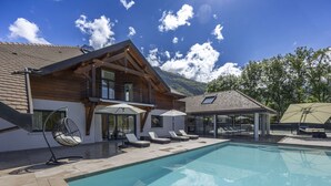 Une maison moderne dotée d’une piscine, d’une façade en bois et d’un balcon avec des chaises longues.