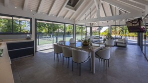 Une salle à manger spacieuse avec un plafond haut, de grandes fenêtres et une vue sur l’extérieur.