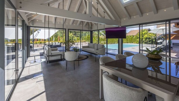 Un vaste espace intérieur doté d’un haut plafond, de grandes fenêtres et d’une vue sur une piscine.