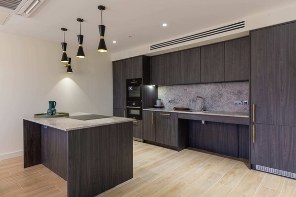Une cuisine moderne avec des meubles de couleur bois foncé, un îlot central et des luminaires suspendus.