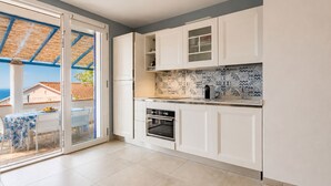 A modern kitchen with white cabinets, a tiled backsplash, and a sliding glass door leading to an outdoor area. - Tra il Borgo e il Mare-Bel Horizonte - Tra il Borgo e il Mare - Bel Horizonte (Capoliveri)