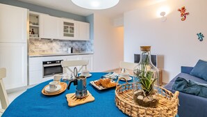 A modern kitchen with white cabinets, a coffee machine, and a dining table set with cups and a plate of food. - Tra il Borgo e il Mare-Bel Horizonte - Tra il Borgo e il Mare - Bel Horizonte (Capoliveri)