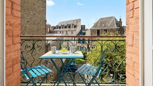 Un balcon avec une table et des chaises, donnant sur une rue bordée d’immeubles.