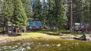 A lodge with a river in front, surrounded by trees. - Gods County Cottage on Swan River (Bigfork)